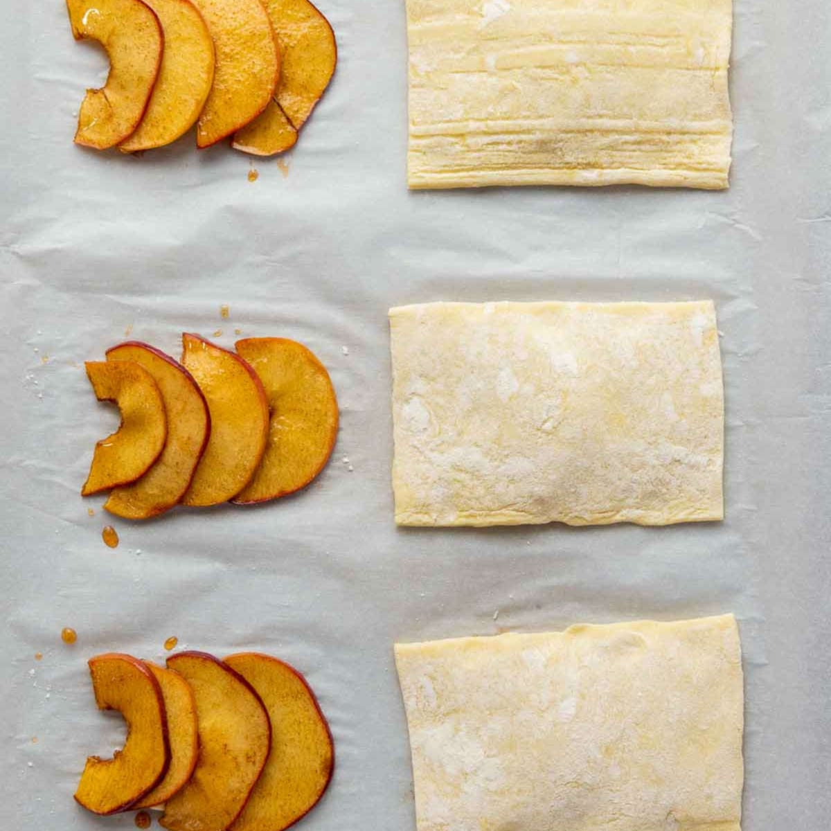 Puff pastry rectangles placed on parchment with caramelized apple slices beside them.