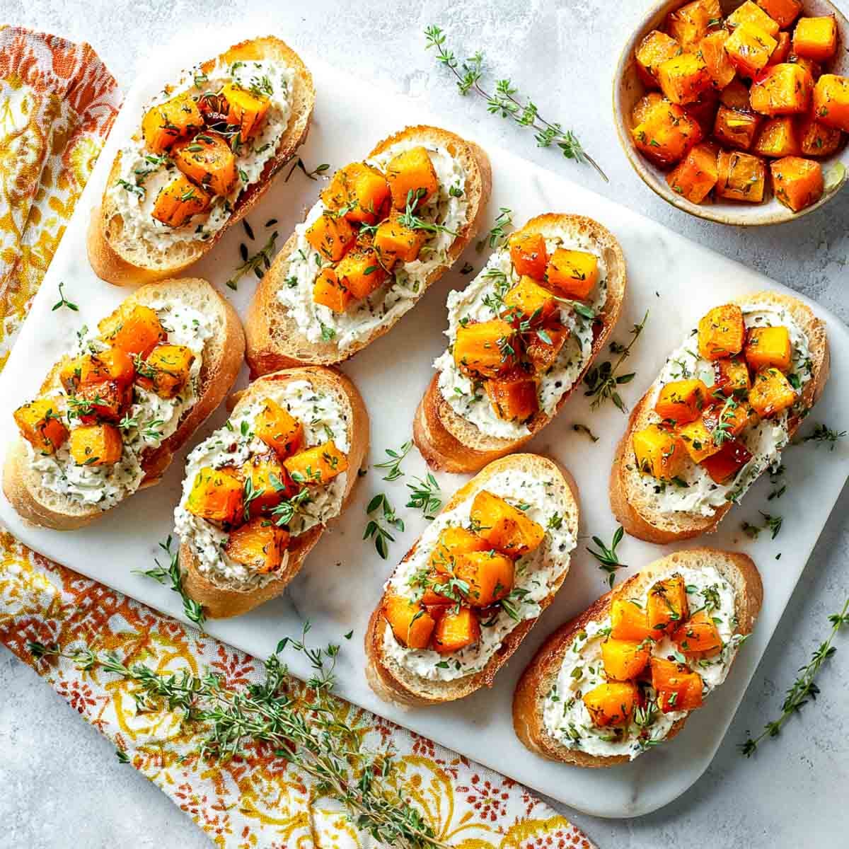 Toasted crostini topped with cashew cream, roasted butternut squash cubes, and fresh herbs.