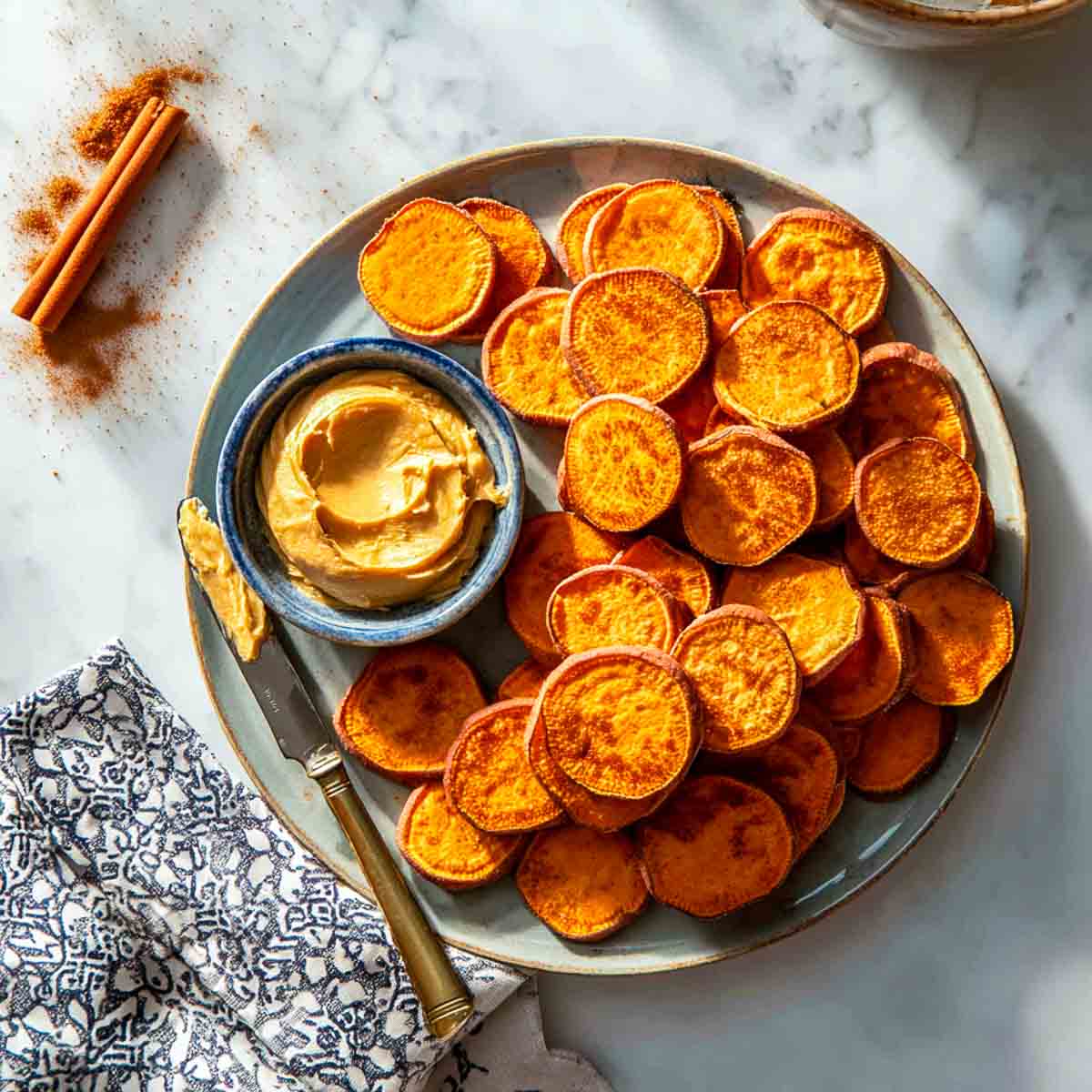 Top-down view of air-fried sweet potato rounds with a bowl of creamy maple butter on marble surface.