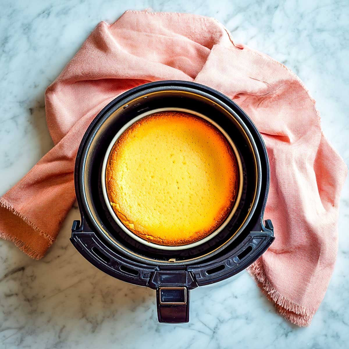 Pumpkin cheesecake baking inside air fryer basket with golden top.