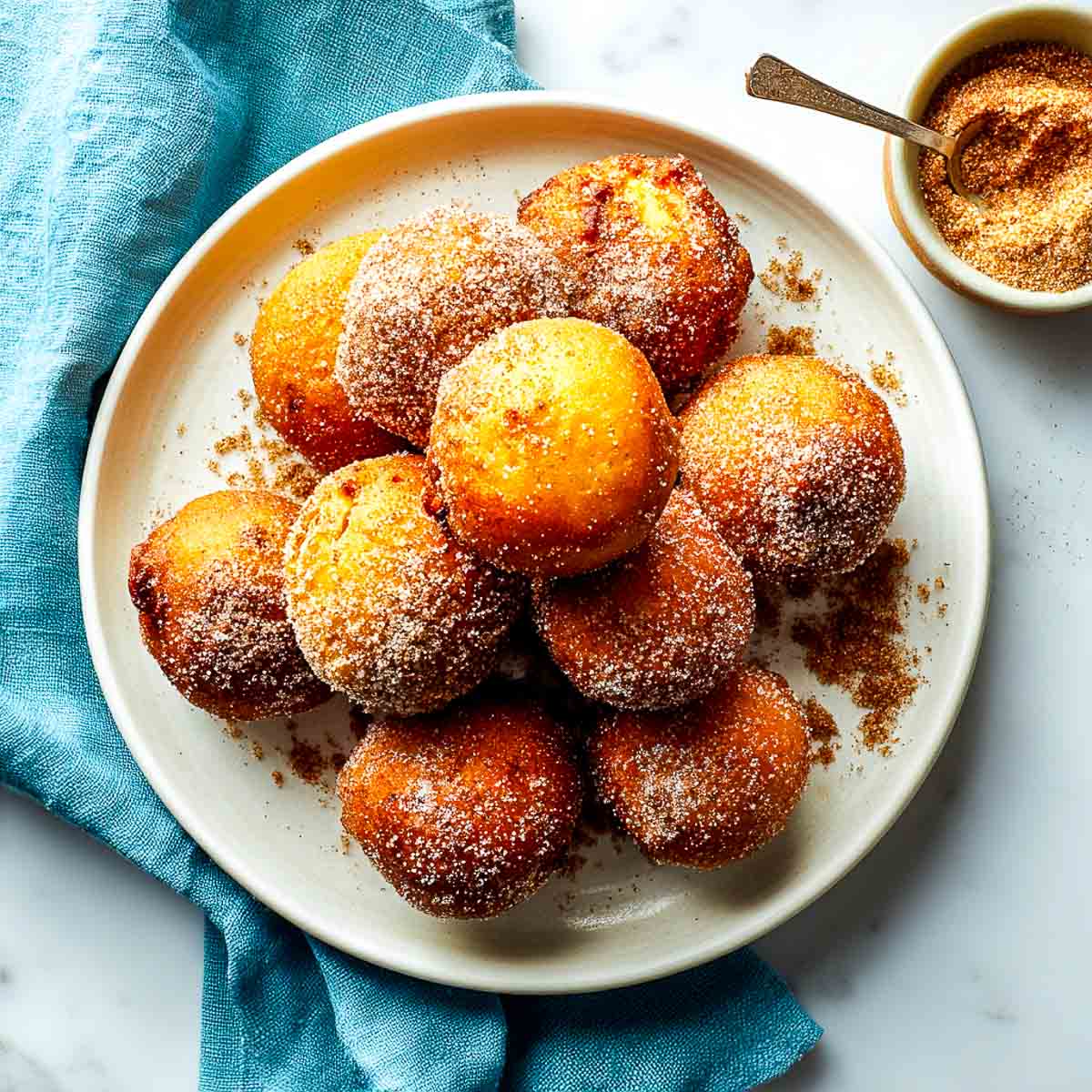 Plate of golden air fryer pumpkin fritters sprinkled with cinnamon sugar.
