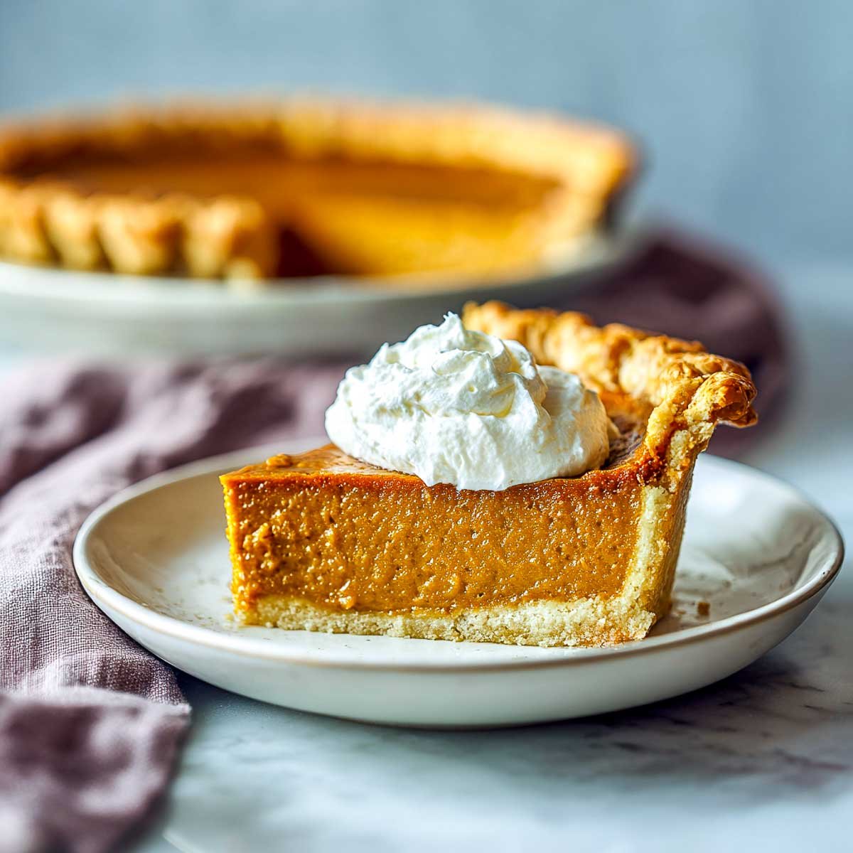 Slice of air fryer pumpkin pie topped with whipped cream.