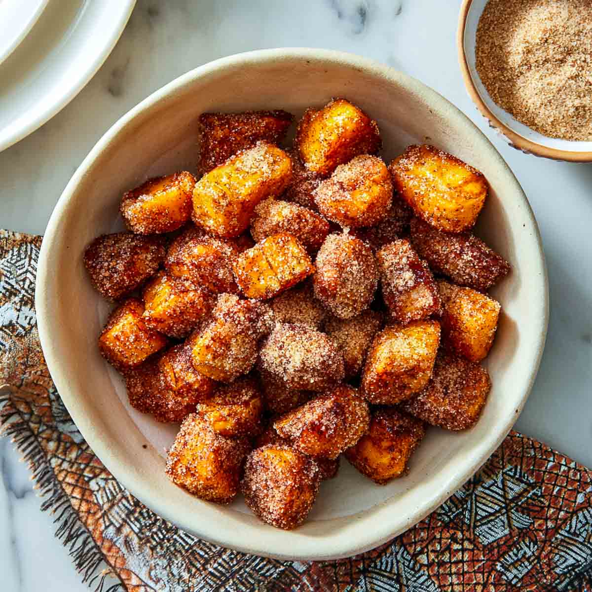 Top-down view of air-fried sweet potato bites coated with cinnamon sugar in a bowl.