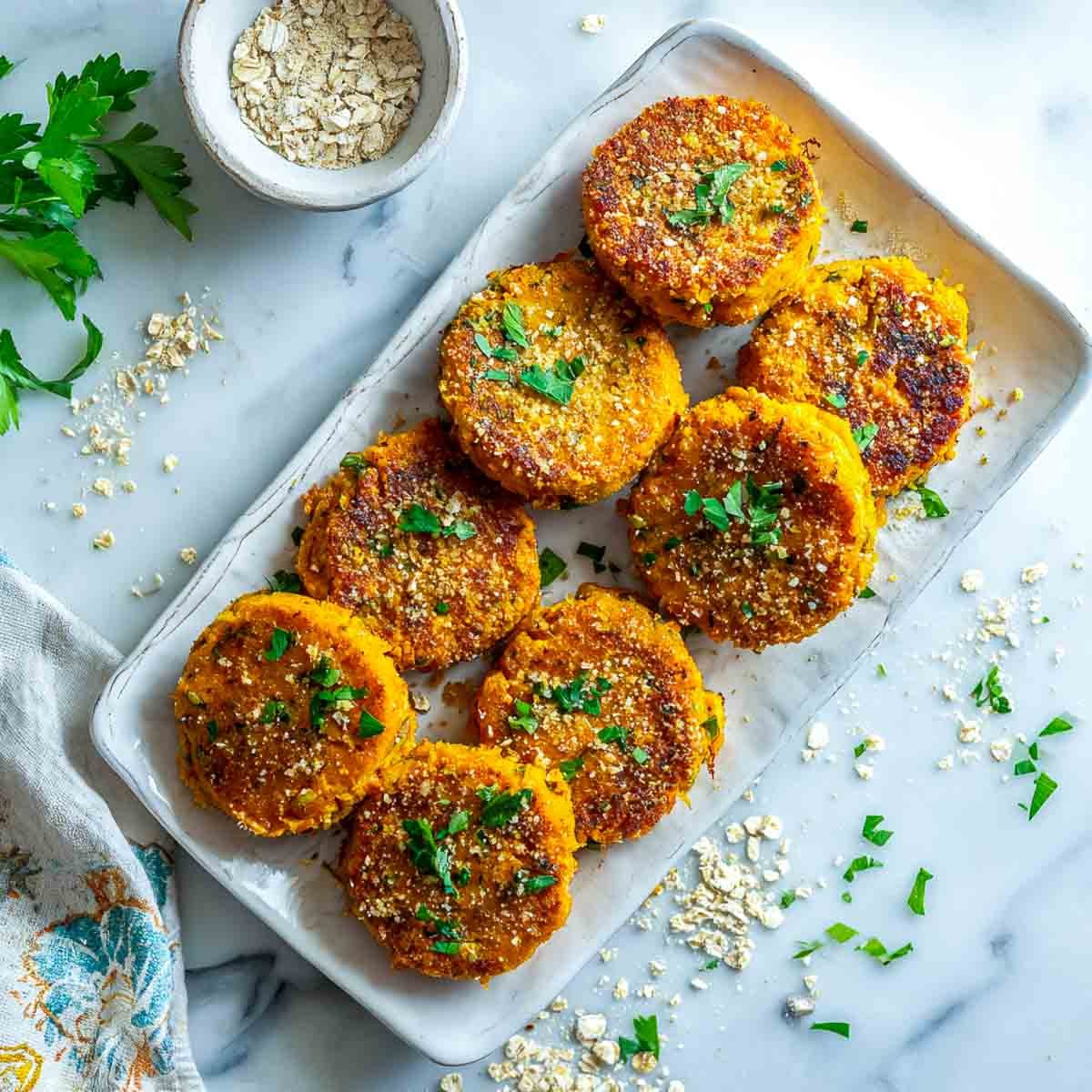 Top-down view of golden air-fried sweet potato patties on a rectangular plate, garnished with parsley and oat crumbs.