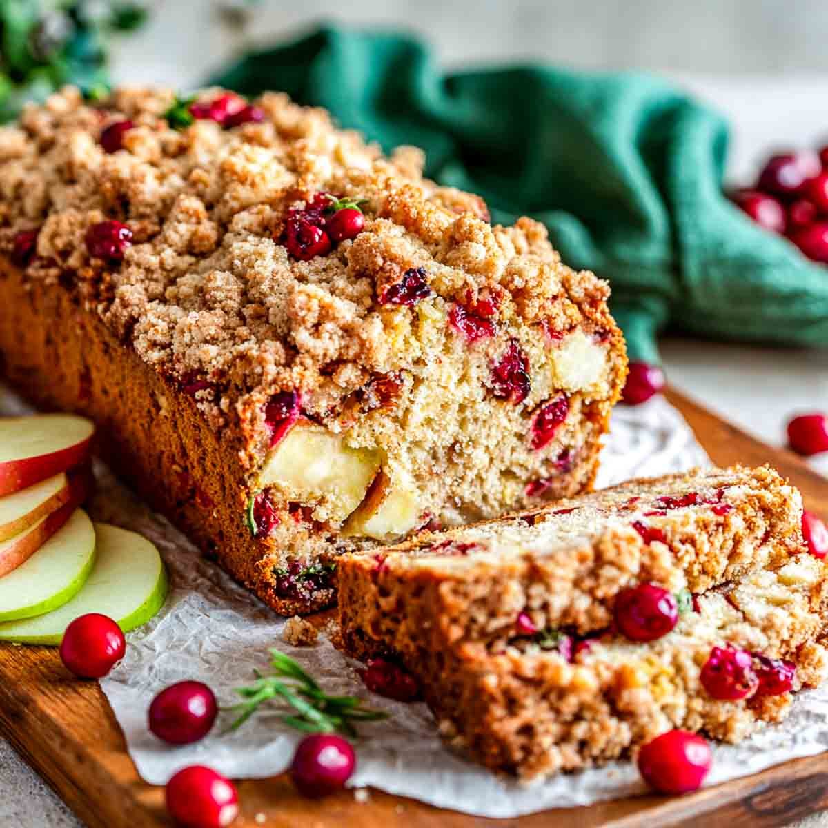 A loaf of apple cranberry bread sliced and placed on a wooden board.