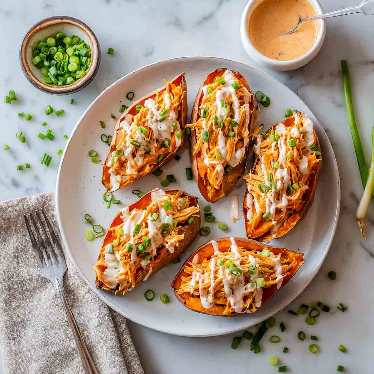 Buffalo turkey stuffed sweet potatoes drizzled with ranch and topped with green onions on a white plate.