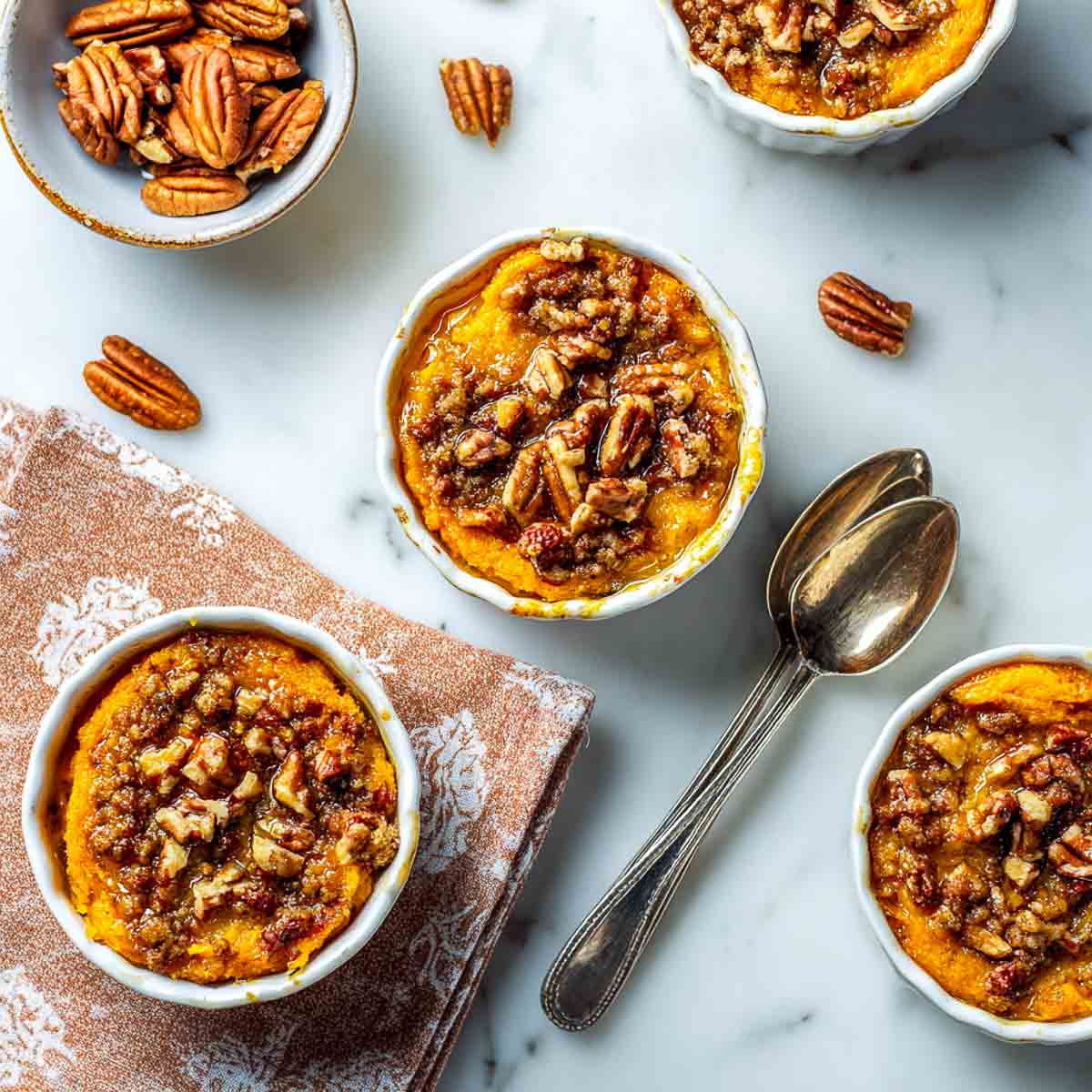 Top-down view of mini sweet potato casserole cups in white ramekins topped with cinnamon pecans on a marble counter.