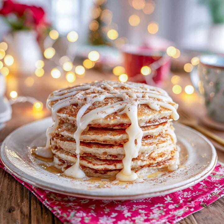 Stack of cinnamon sugar pancakes drizzled with vanilla glaze and surrounded by soft Christmas lights on a red napkin.