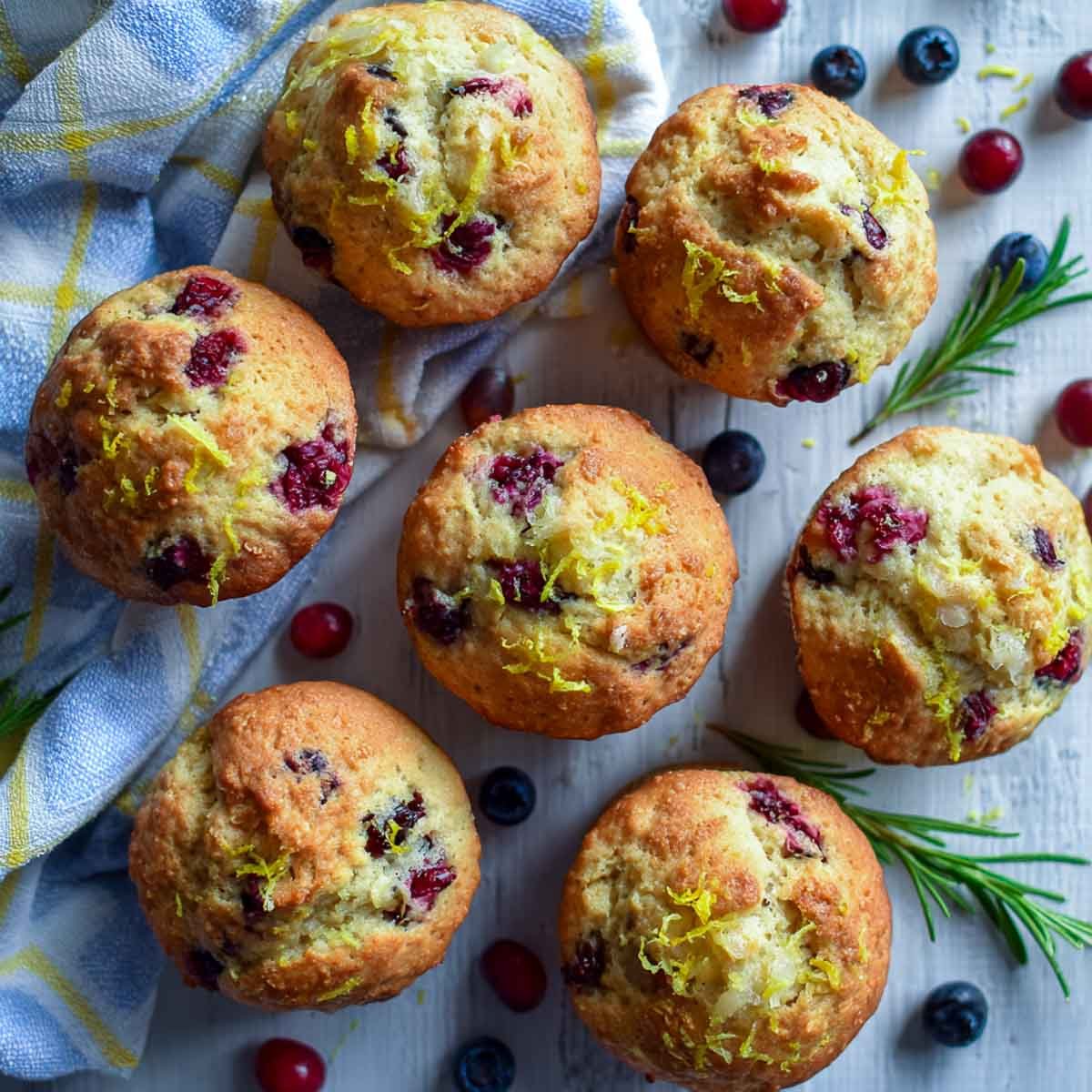 Cranberry blueberry muffins on white wood surface.