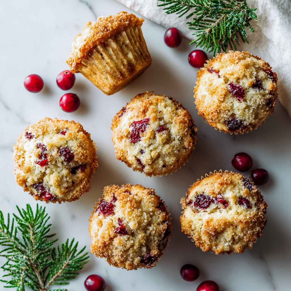 cranberry and orange muffins with brown sugar crust on marble counter.