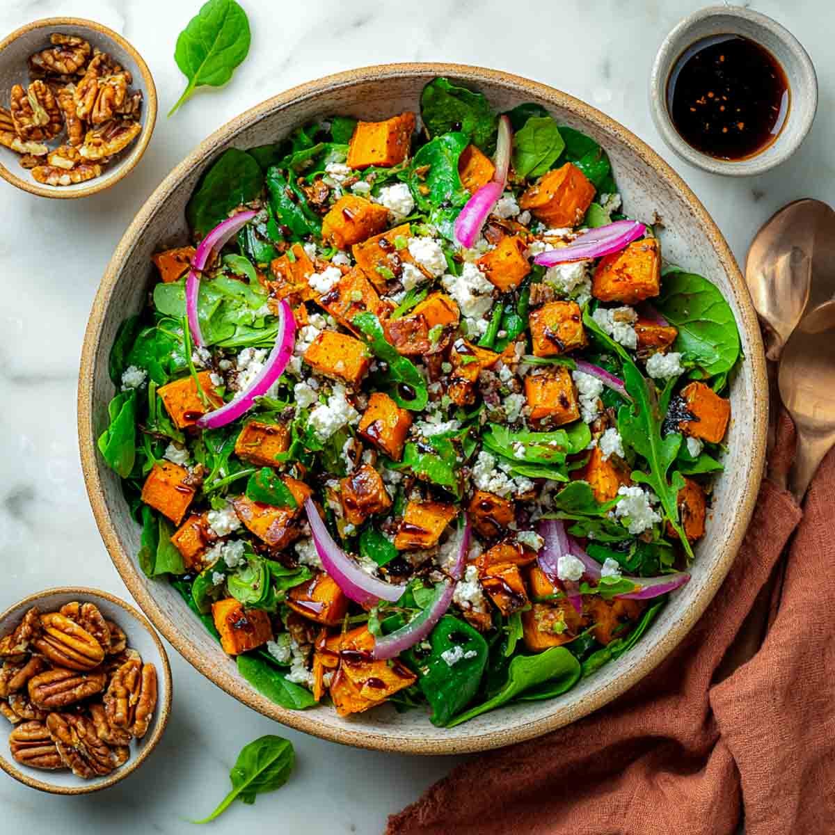Air-fried sweet potato salad with greens, feta, red onions, pecans, and balsamic glaze in a rustic bowl.