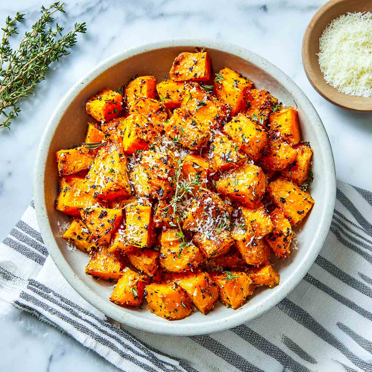 Top-down view of golden air-fried sweet potato cubes topped with parmesan and thyme in a bowl.