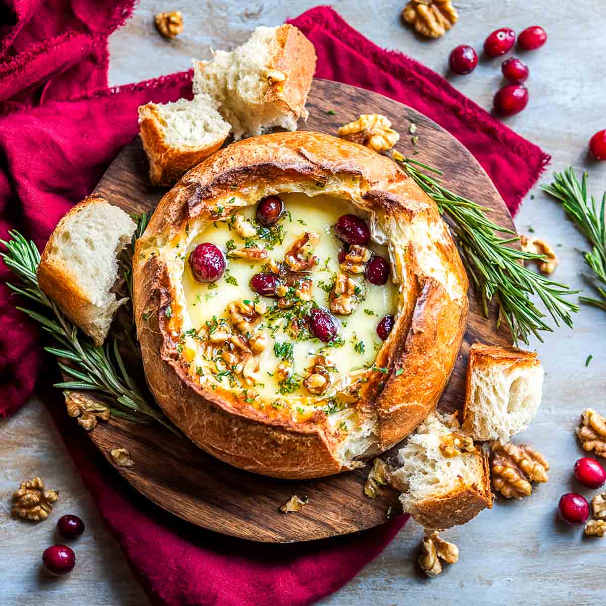 Bread bowl with cranberry and brie dip on a wooden board.