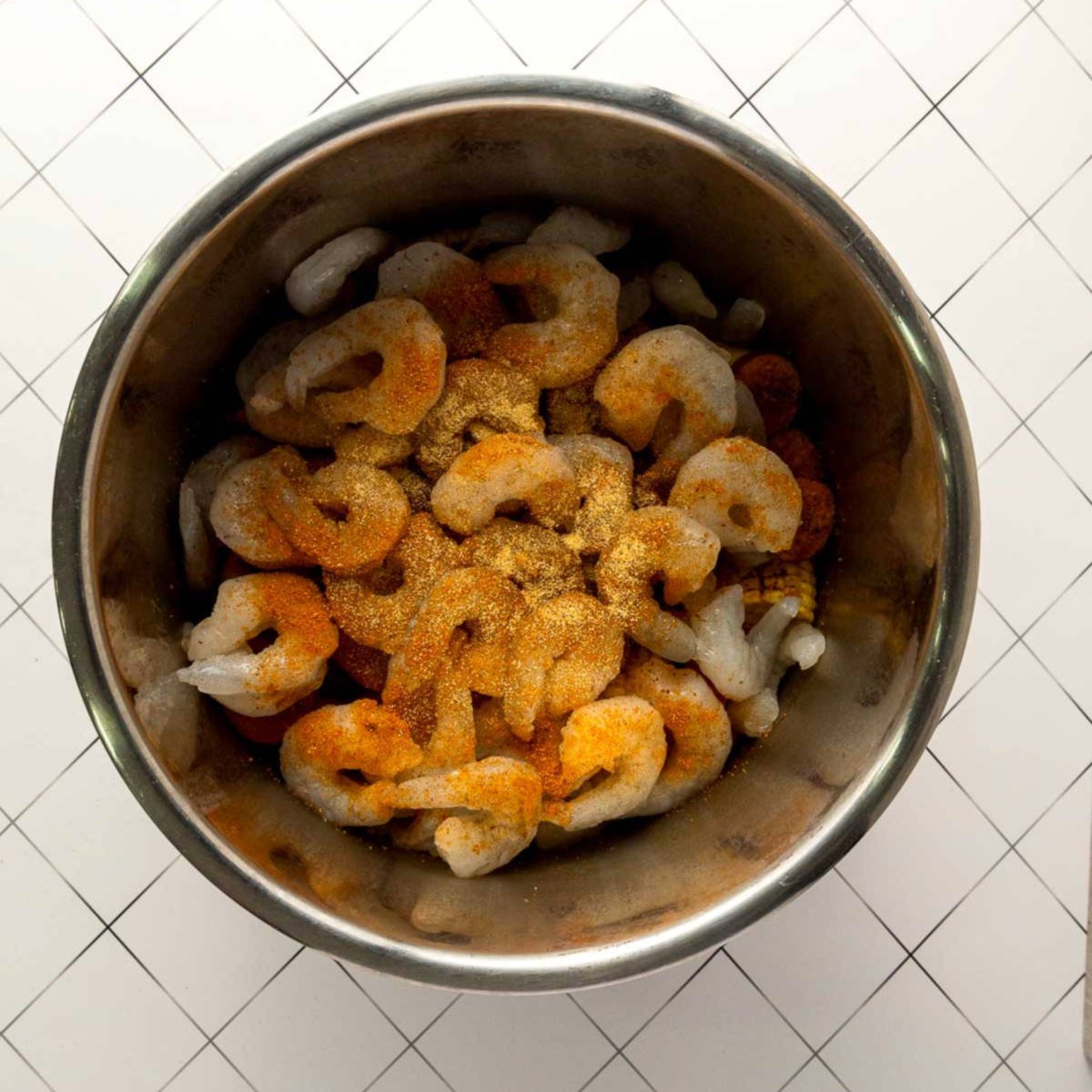 Raw shrimp layered on top with seasoning inside Instant Pot.