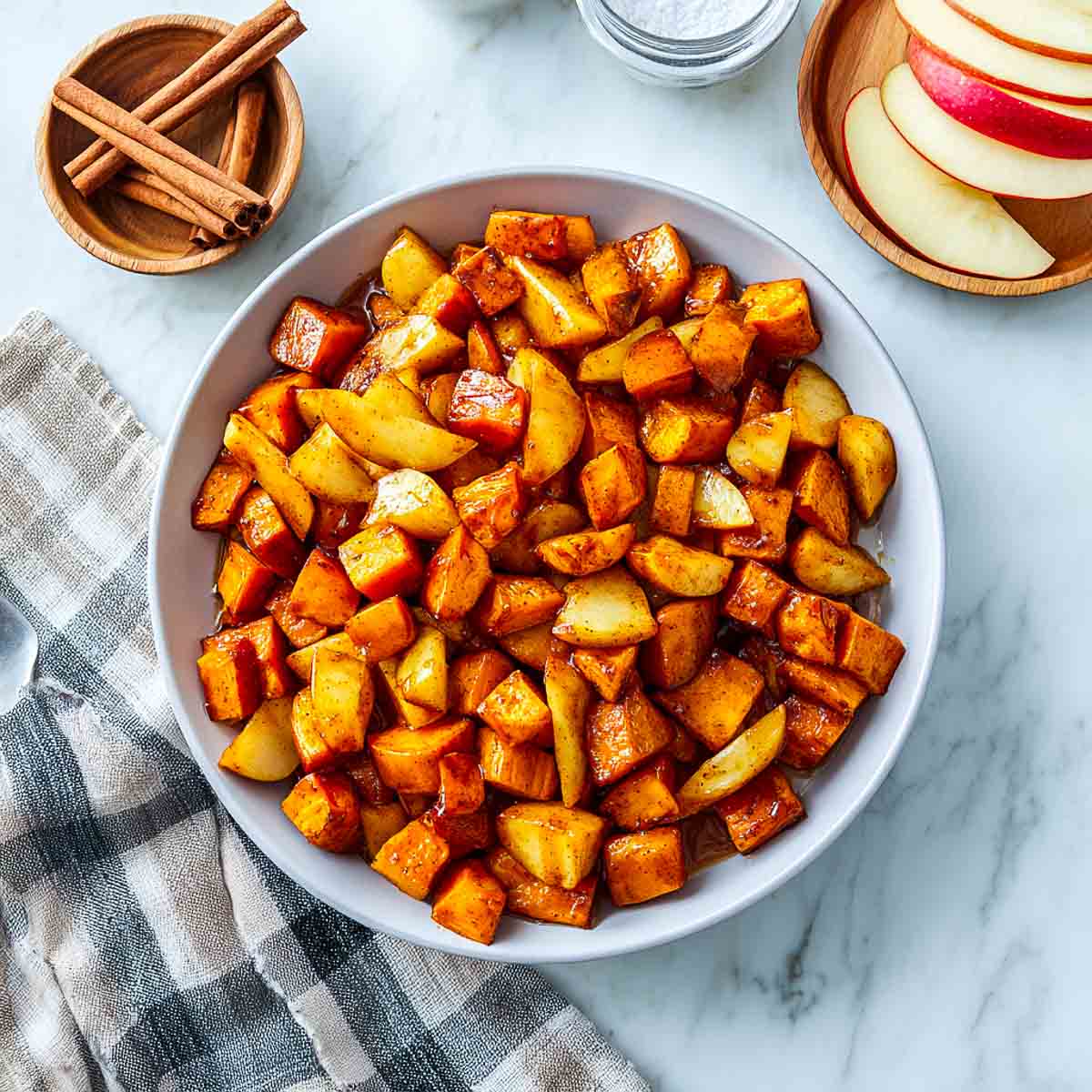 Top-down view of air-fried sweet potato cubes mixed with cinnamon apples in a white bowl with cinnamon sticks nearby.