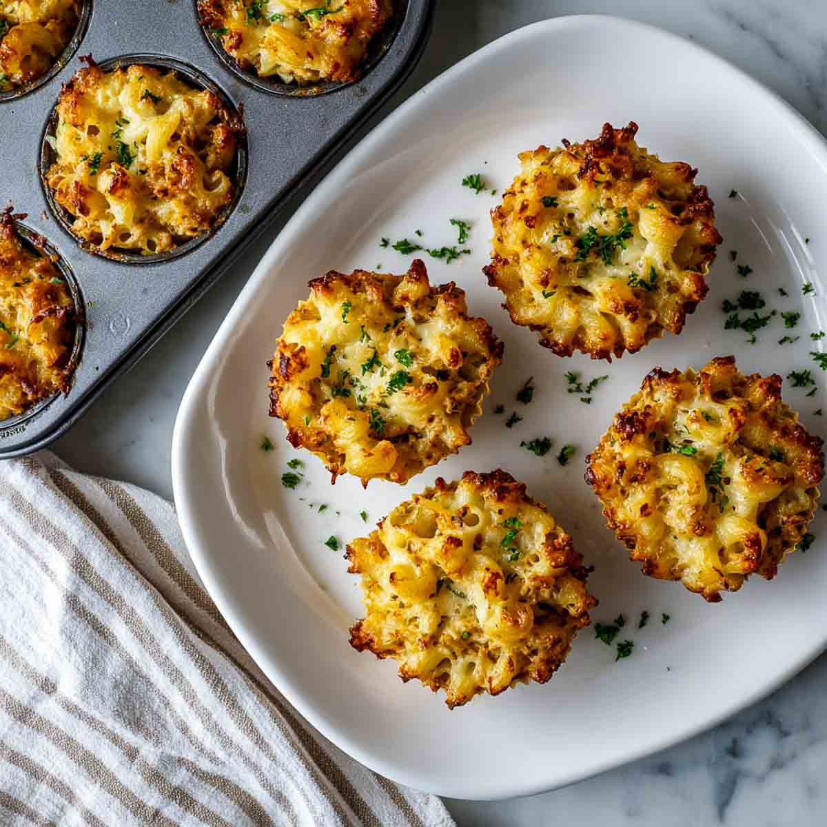 Angled view of baked leftover turkey mac and cheese cups on a plate with golden tops.