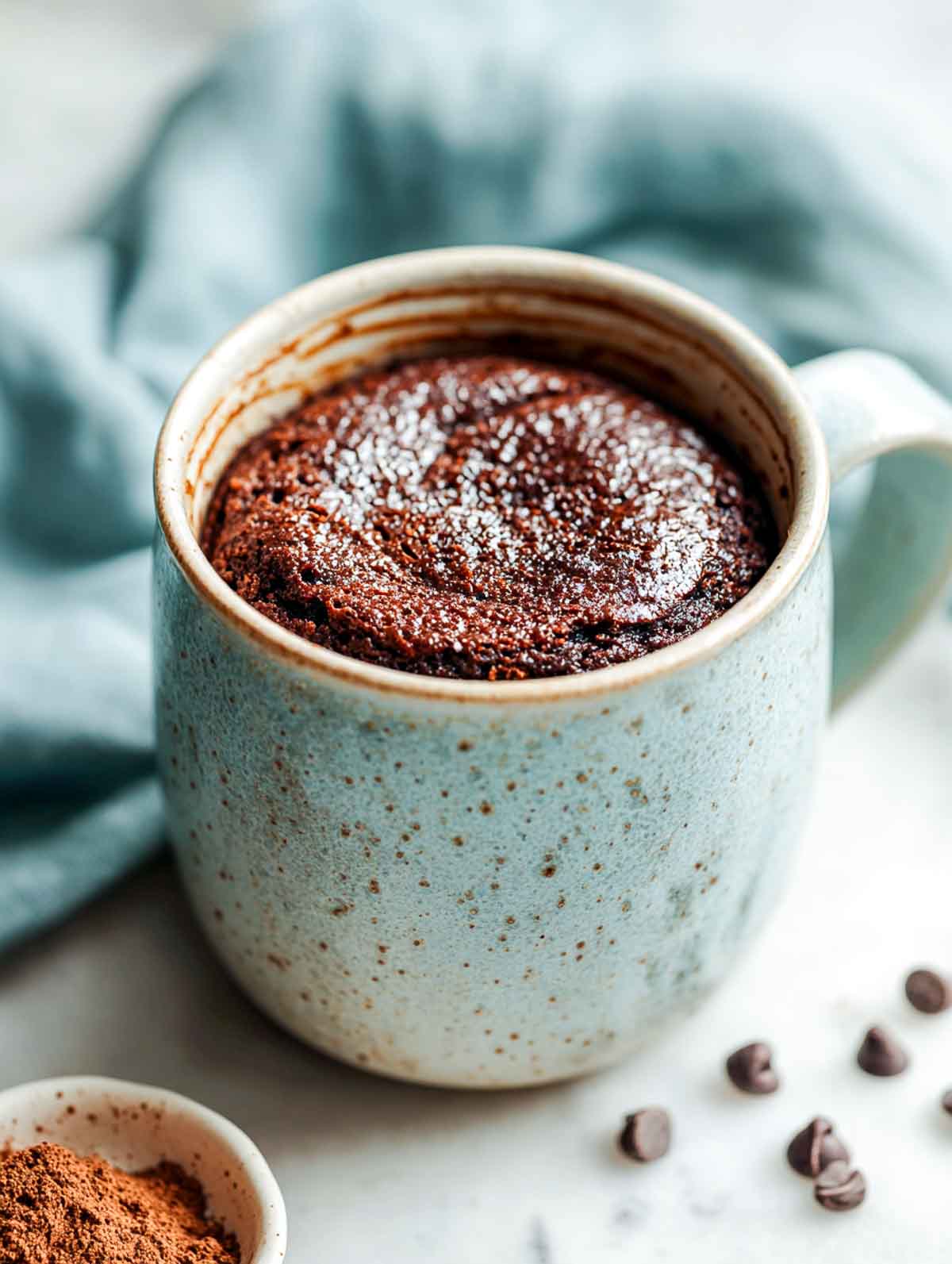 A top-down view of a warm, fudgy cottage cheese brownie mug cake in a speckled ceramic mug.