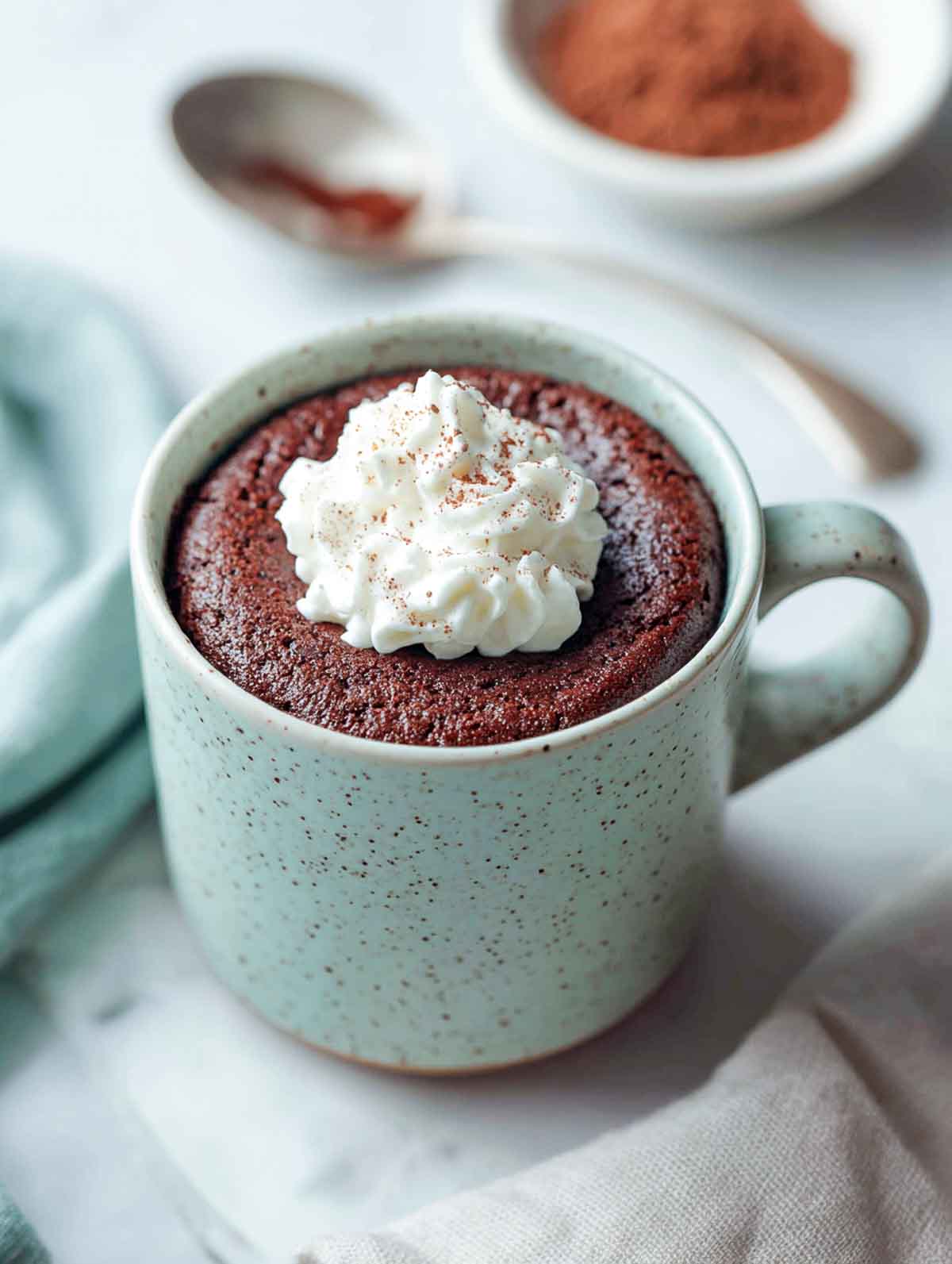 An angled view of a keto chocolate mug cake in a speckled mug topped with whipped cream.