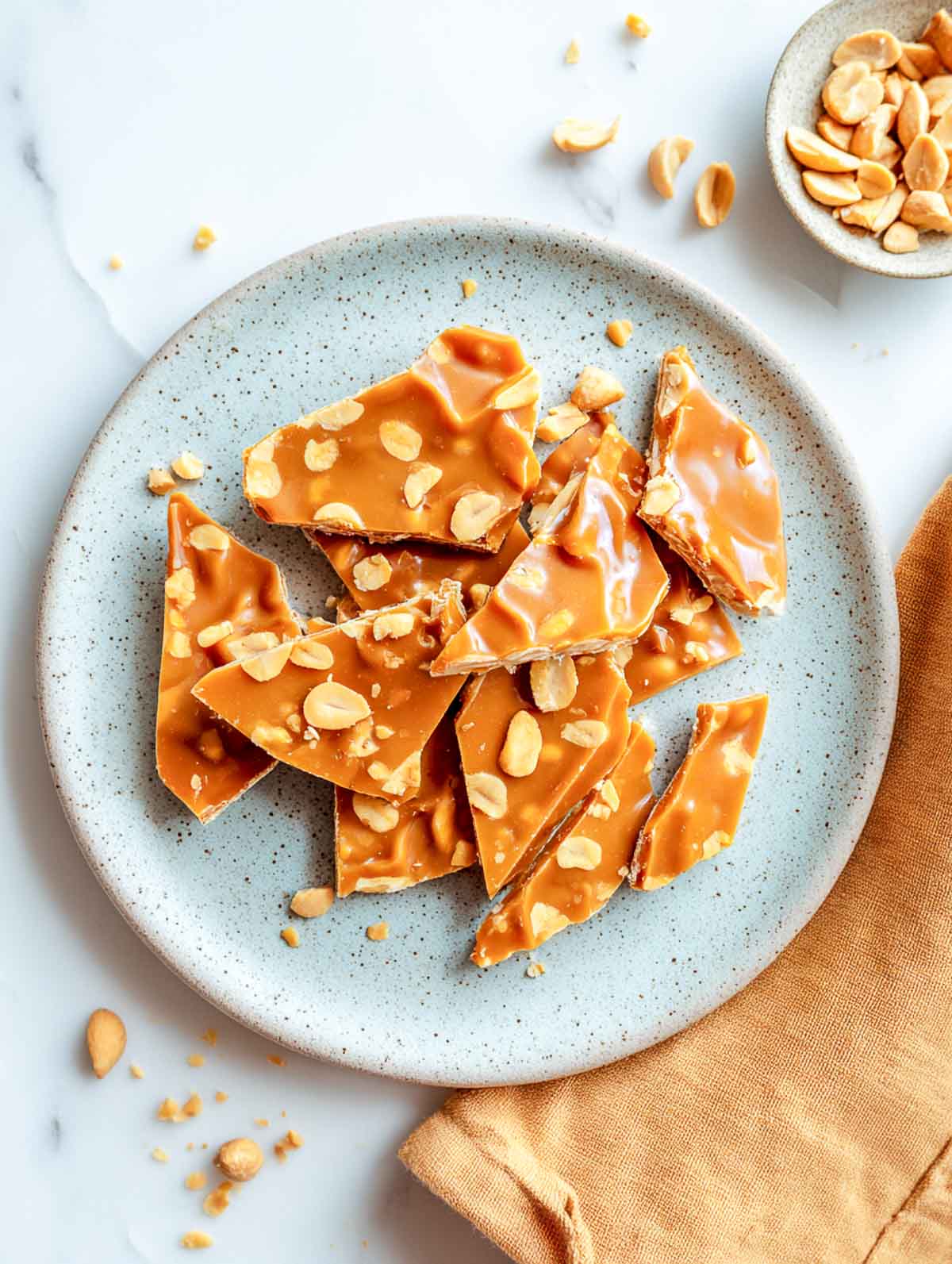 Golden microwave peanut brittle broken into rustic shards on speckled plate.