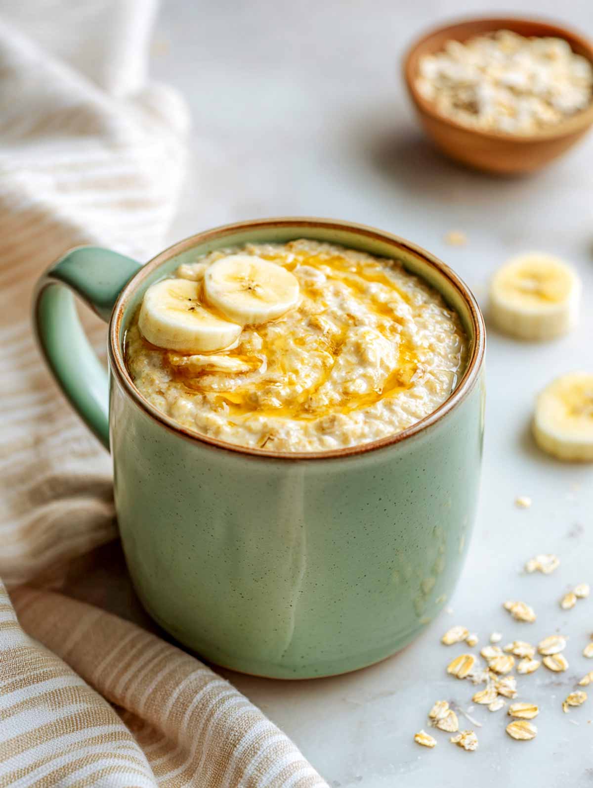 Banana bread oatmeal in a sage green mug topped with banana slices.