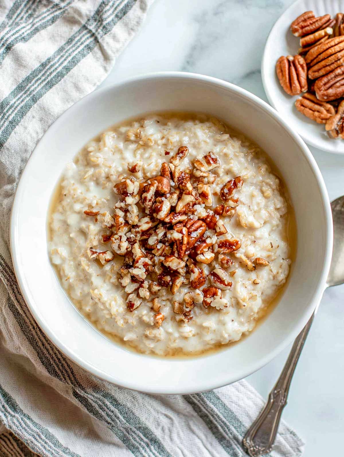 Warm maple pecan oatmeal topped with chopped toasted pecans in a white bowl.