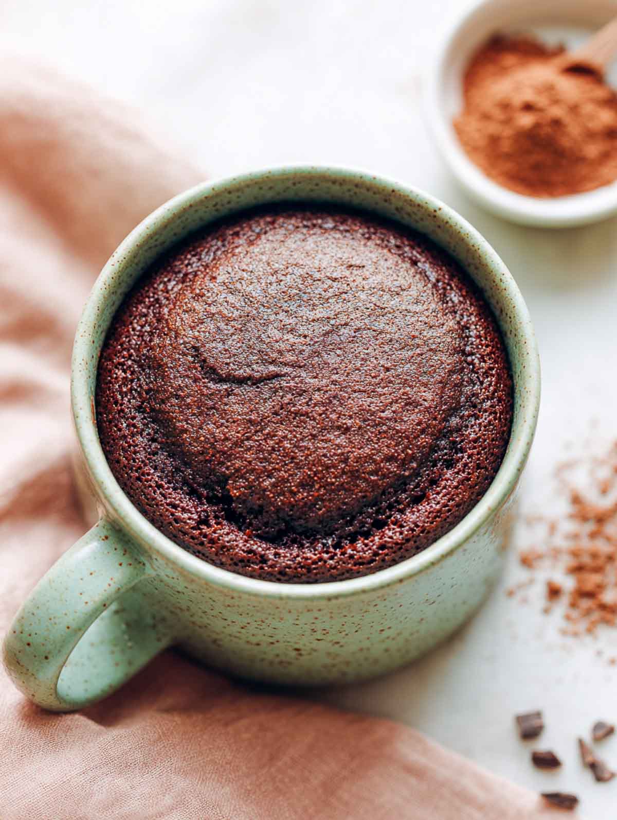 Simple chocolate mug cupcake in muted sage green mug on marble surface.