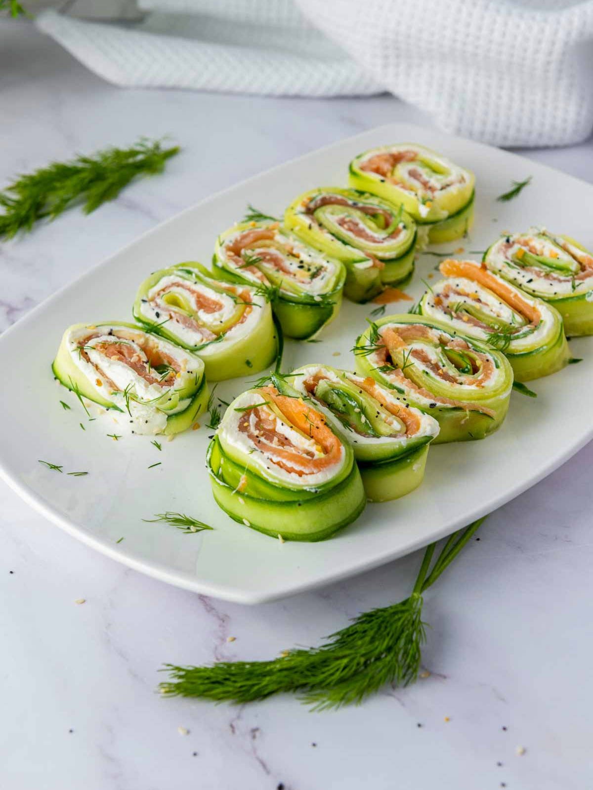 Side view of cucumber smoked salmon roll ups served on a white plate.