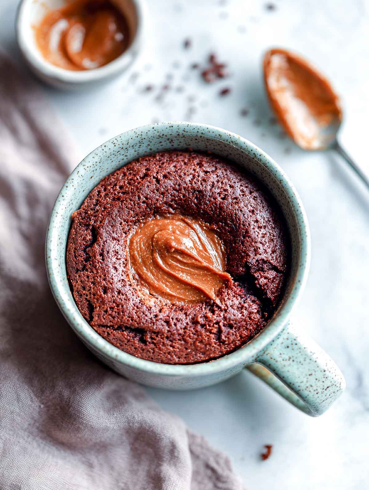A top-down view of a keto chocolate brownie mug cake with a molten almond butter center in a speckled mug.