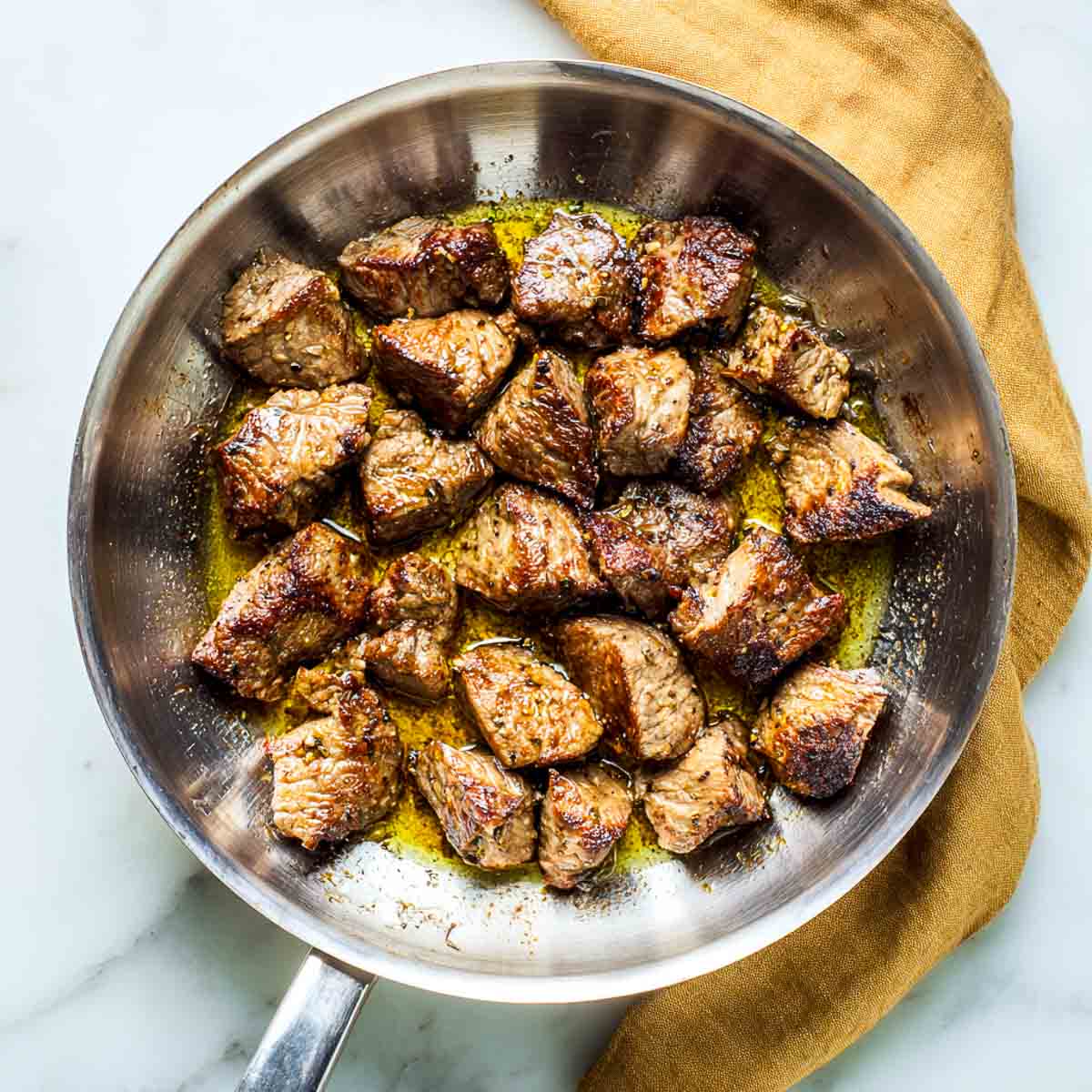 Lamb pieces searing in a stainless steel pan until browned.