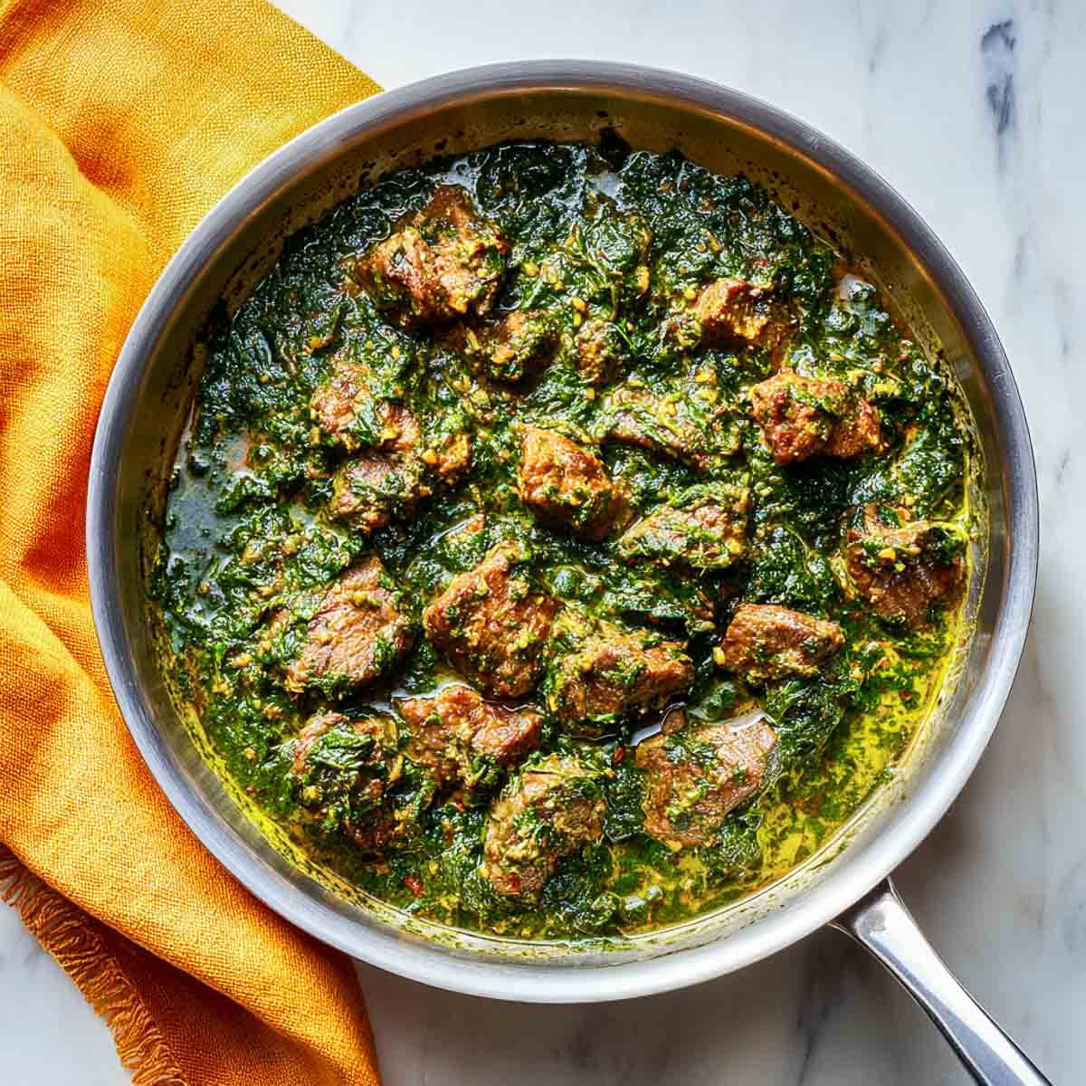 Lamb pieces simmering in a spinach gravy in a stainless steel pan.