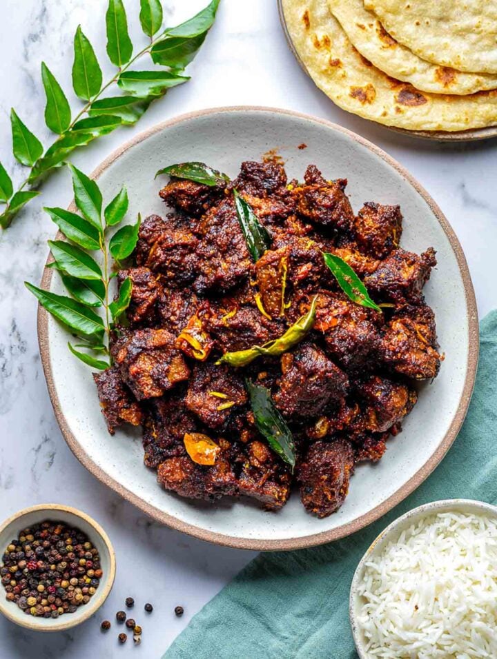 Dry lamb pepper fry served on a white plate with curry leaves.