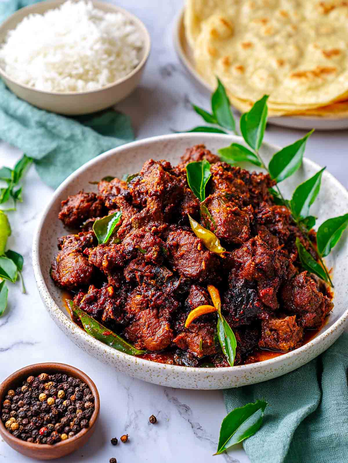 Spicy lamb pepper fry piled high in a bowl with fresh curry leaves.