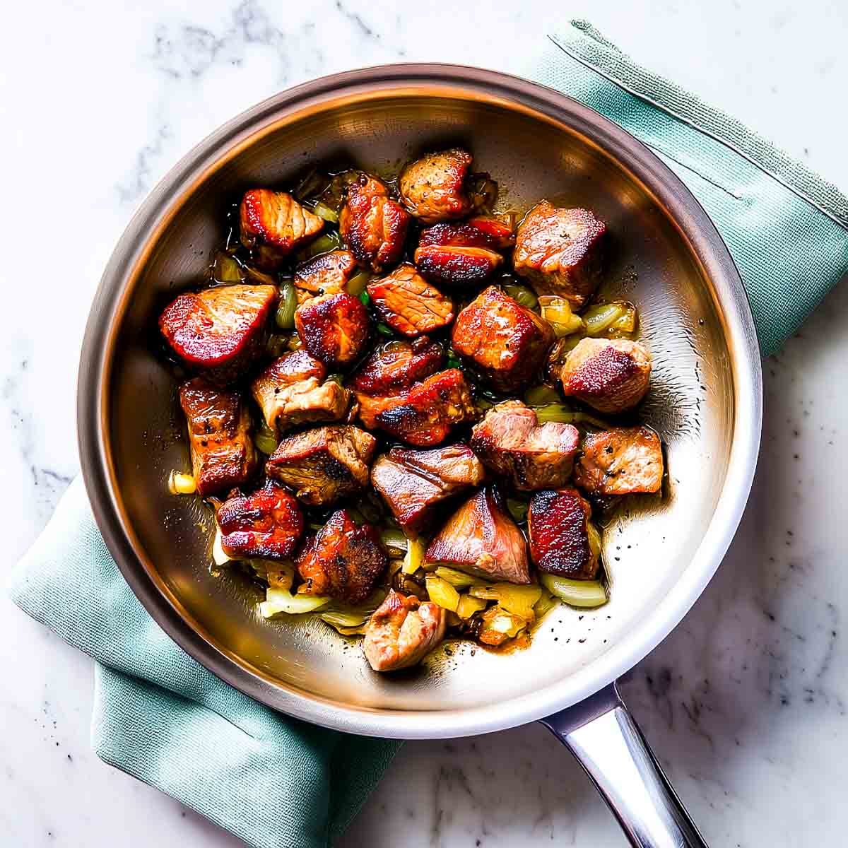 Browned lamb cubes cooking over sautéed onions in a stainless steel pan.