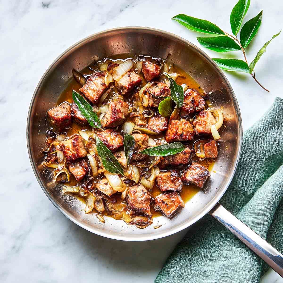 Lamb simmering with onions in a stainless steel pan with added water.