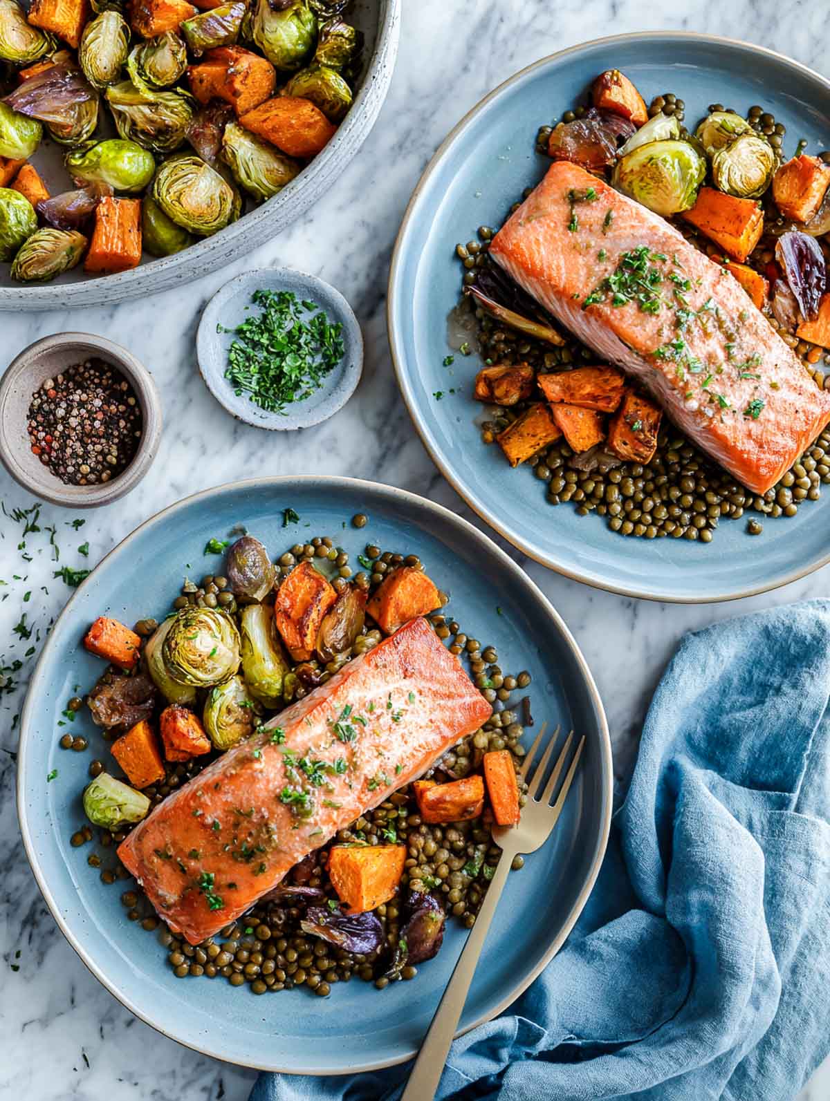 Lentils and winter veggies salmon fillets with a bowl of roasted vegetables in the background.