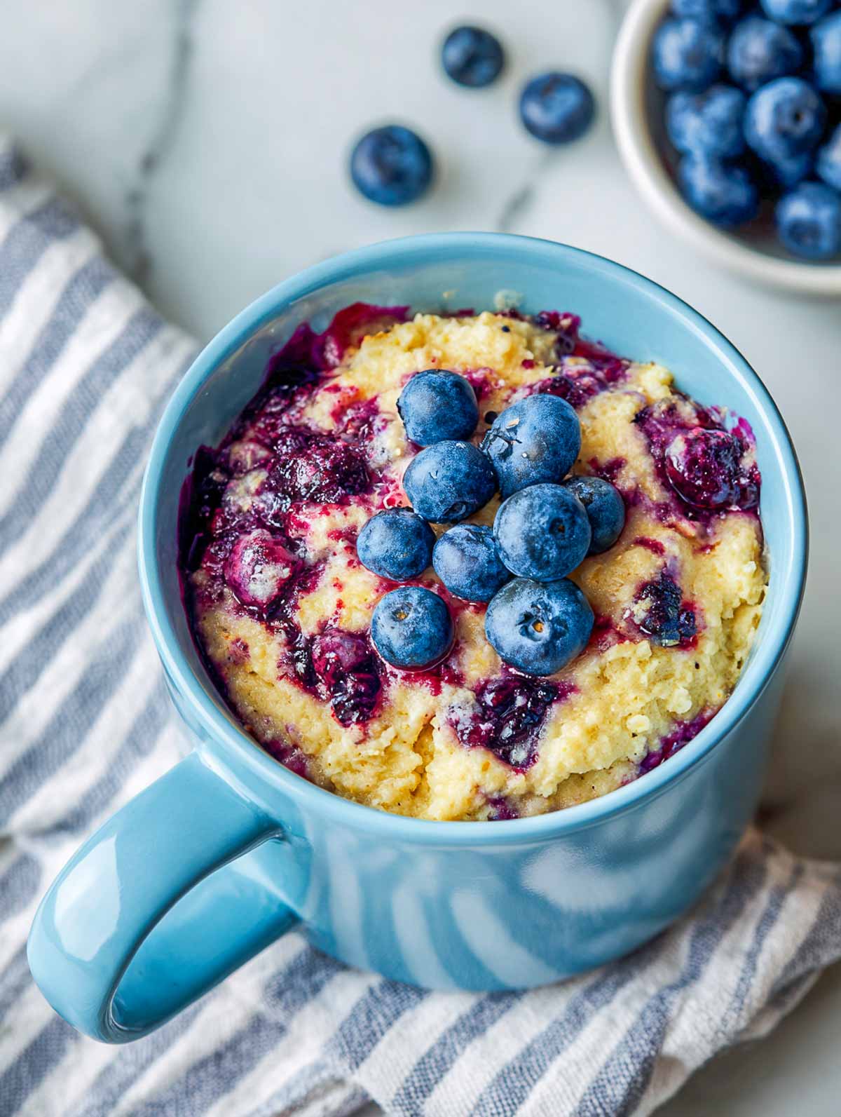 Blueberry muffin microwave oatmeal in a blue mug with fresh blueberries on top.