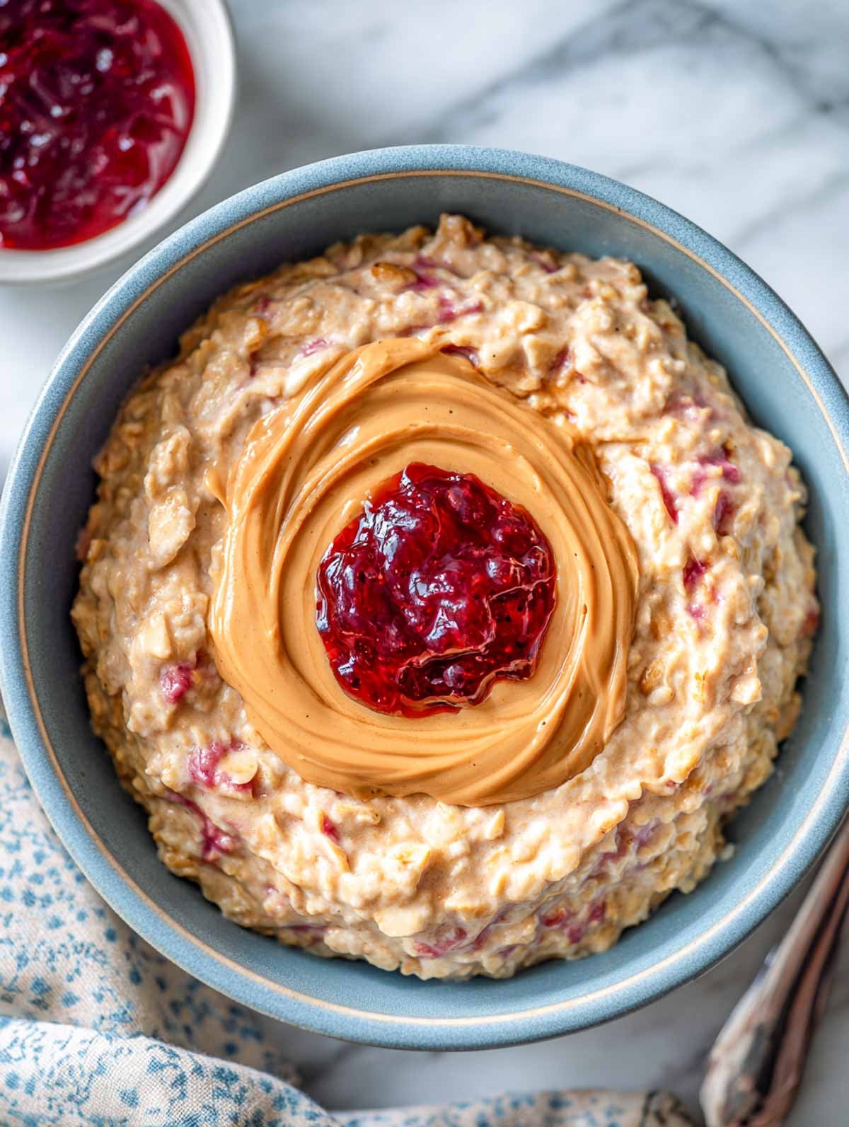 Creamy peanut butter jelly oatmeal with marbled berries in a blue bowl.