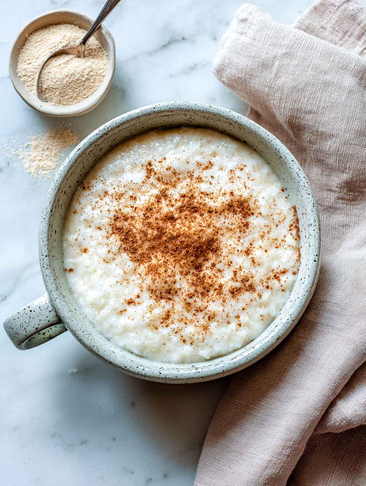 A top-down view of creamy microwave rice pudding topped with cinnamon in a speckled mug.