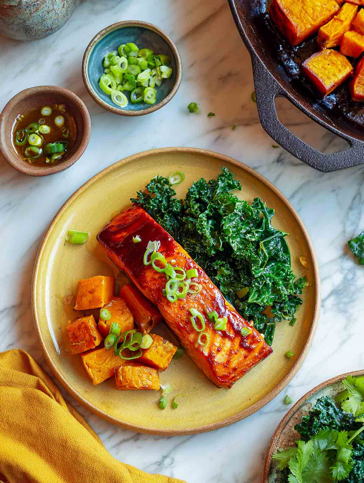 Chipotle-glazed salmon with roasted sweet potatoes and sautéed kale on yellow plate.