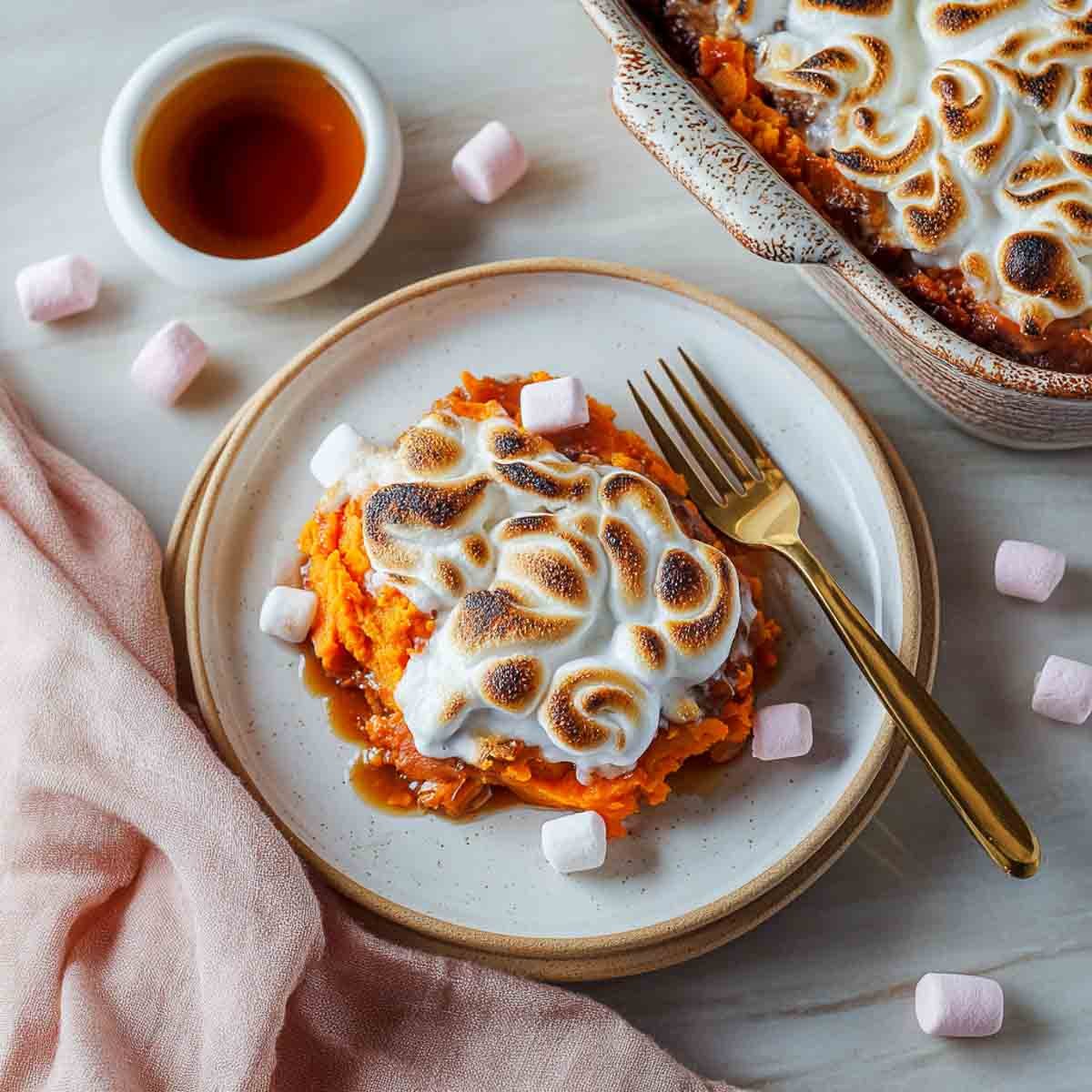 Top-down view of a plated serving of sweet potato casserole topped with toasted marshmallow swirls and maple drizzle, with the baking dish in the corner.