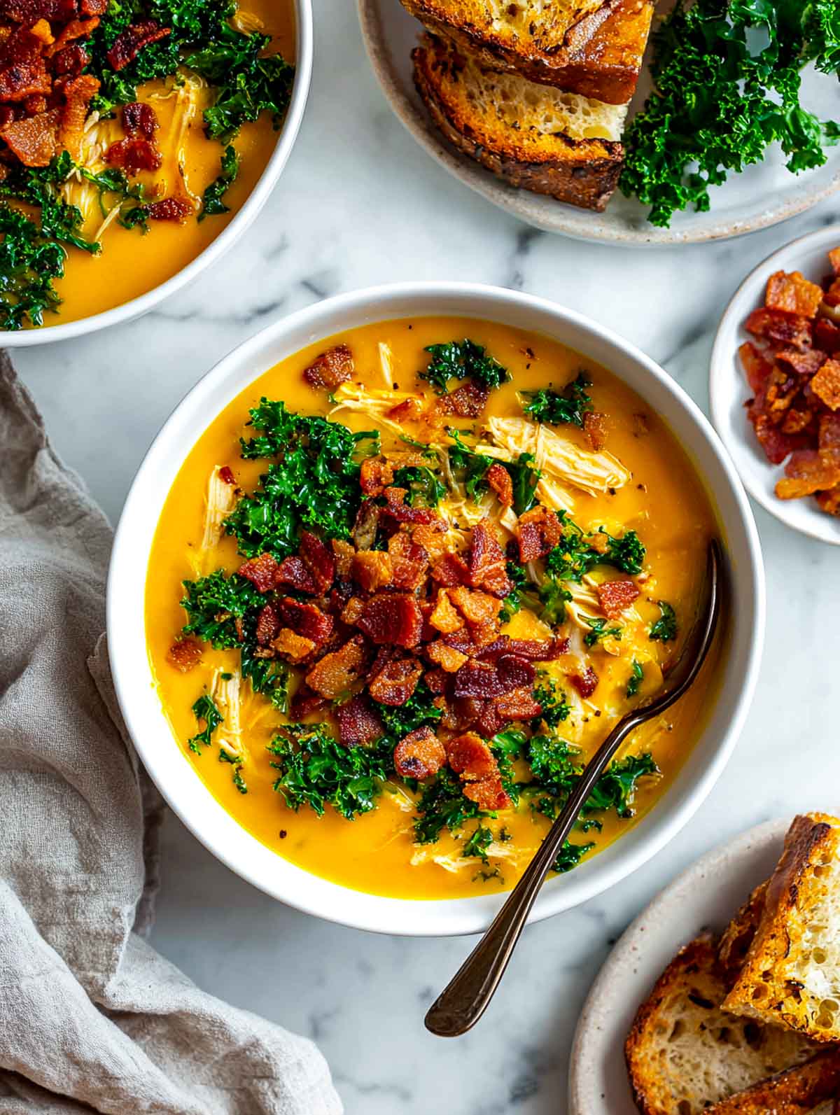 Creamy sweet potato soup with shredded chicken, kale, and crispy bacon crumbles served with toasted bread on a marble surface.