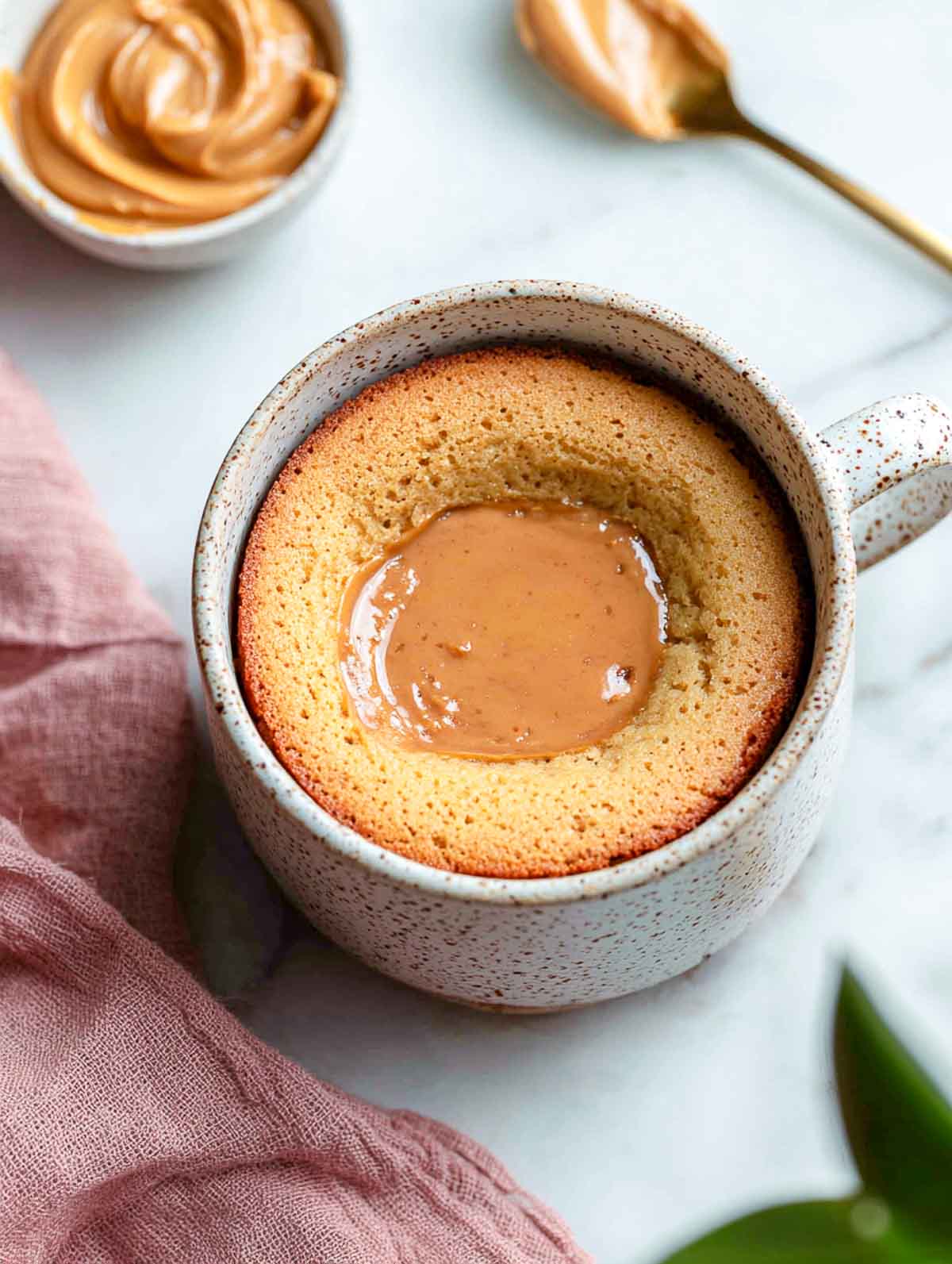 A top-down view of a vegan peanut butter lava cake in a speckled mug with a soft molten peanut butter center.