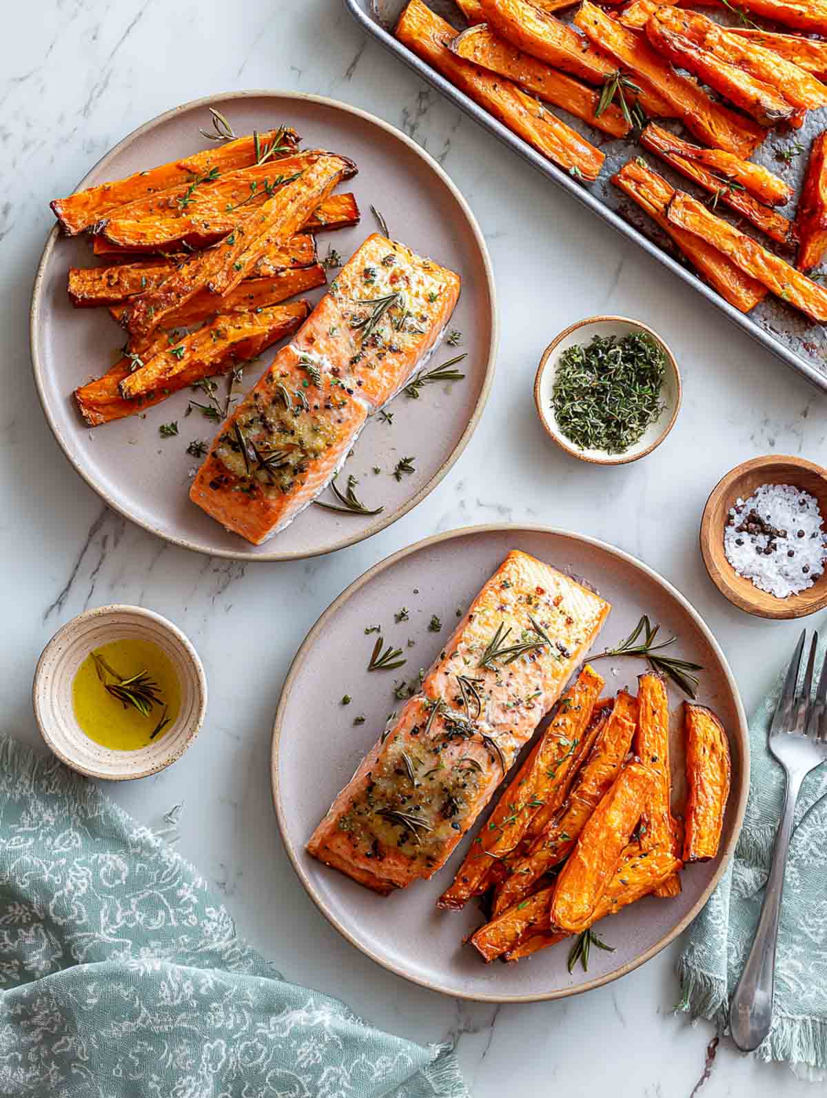 Herb-roasted salmon fillets served with roasted sweet potato batonettes on plates.