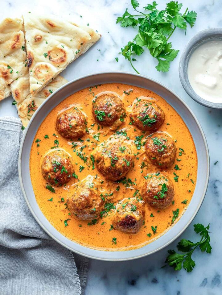 Creamy Indian lamb meatballs served in orange curry sauce with naan.
