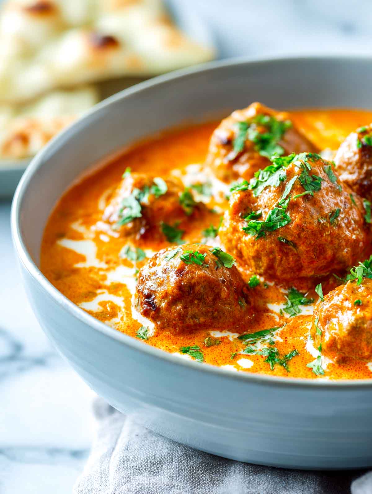 Close-up of lamb meatballs in creamy orange curry garnished with herbs.