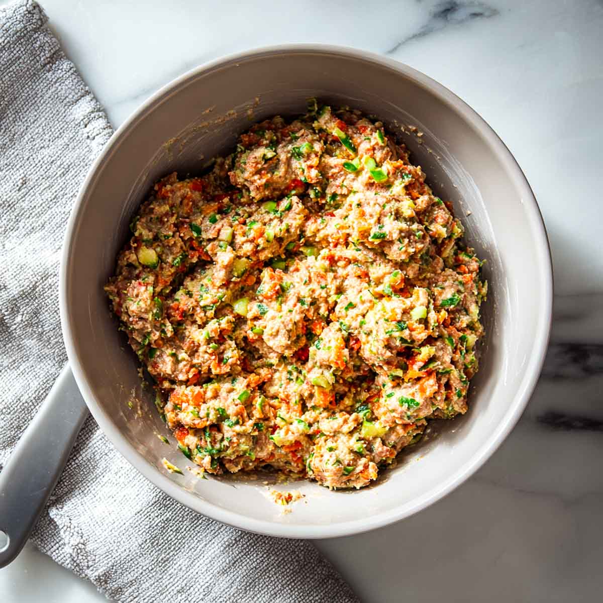 Lamb meatball mixture with vegetables combined in a large mixing bowl.