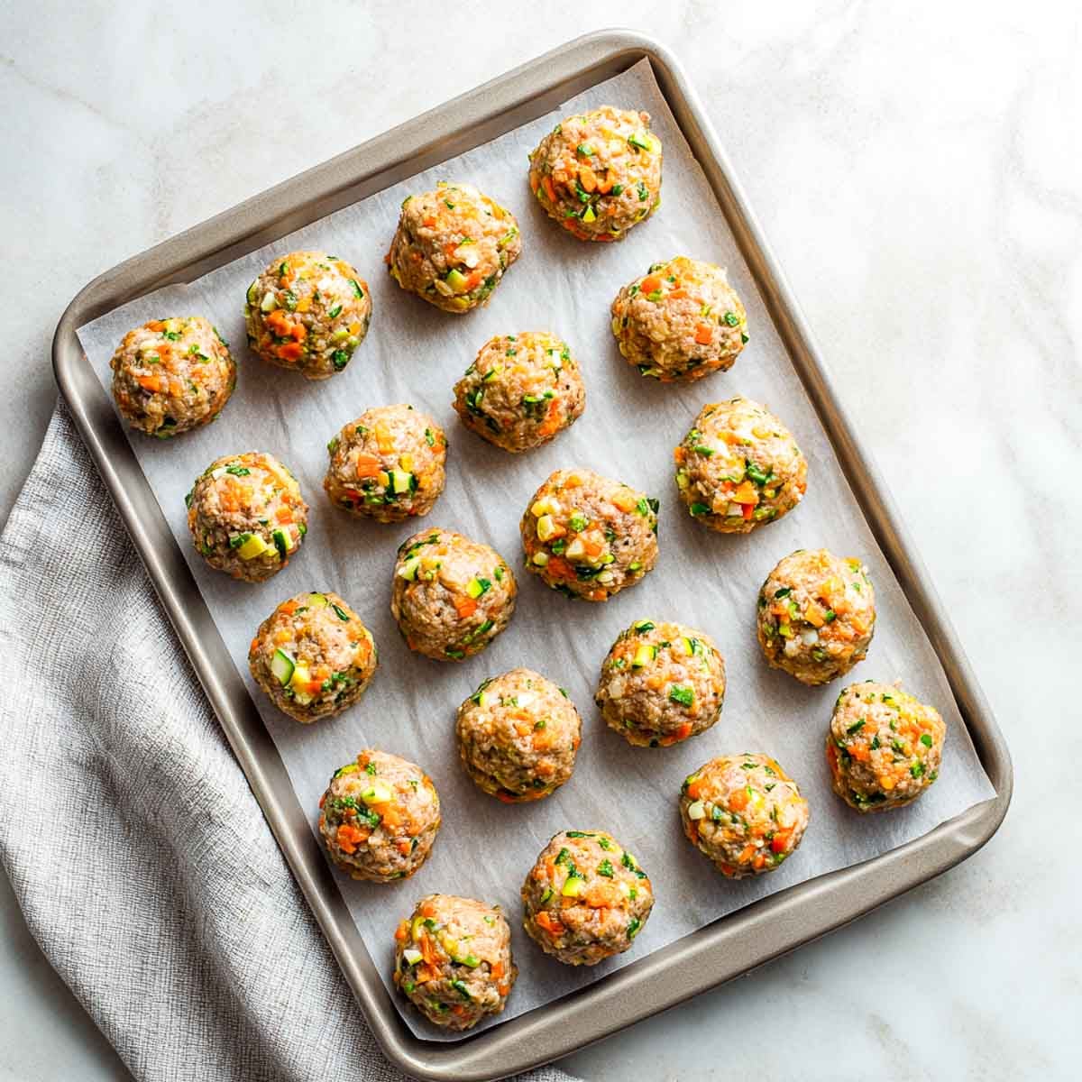 Twenty raw lamb meatballs arranged evenly on a parchment-lined baking tray.