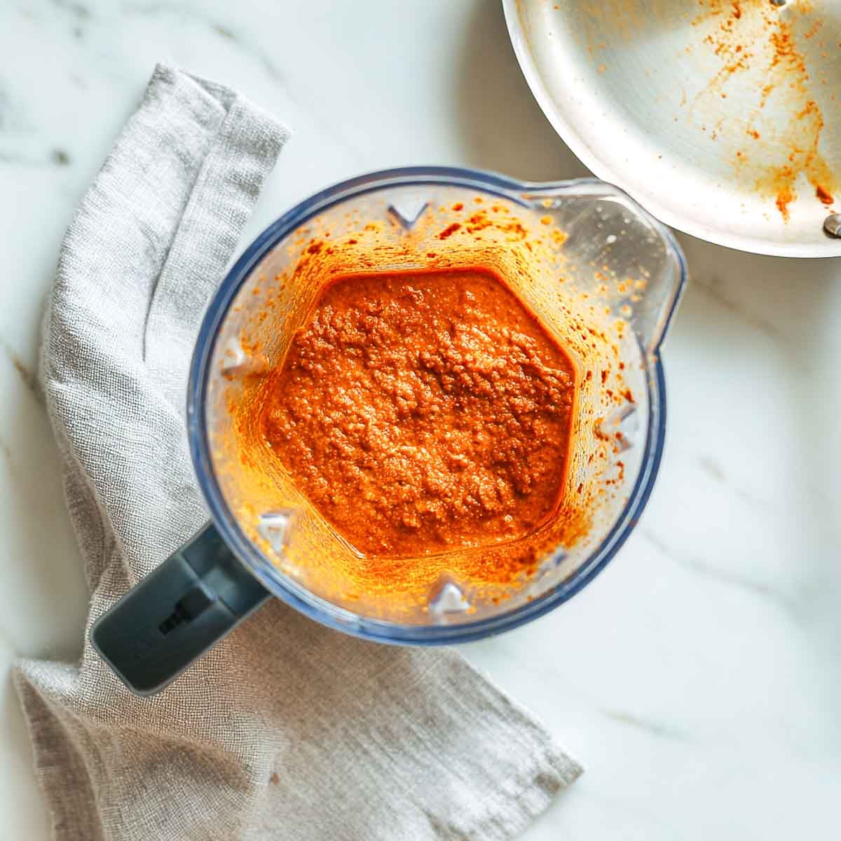 Blended orange curry mixture inside a blender jar on marble countertop.