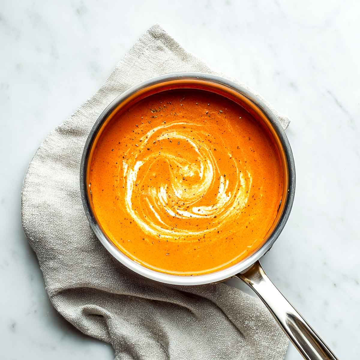 Smooth orange curry sauce with cream swirls in a stainless steel pan.