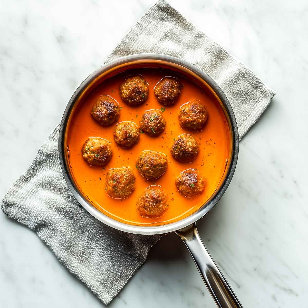 Lamb meatballs arranged on top of silky orange curry sauce in pan.